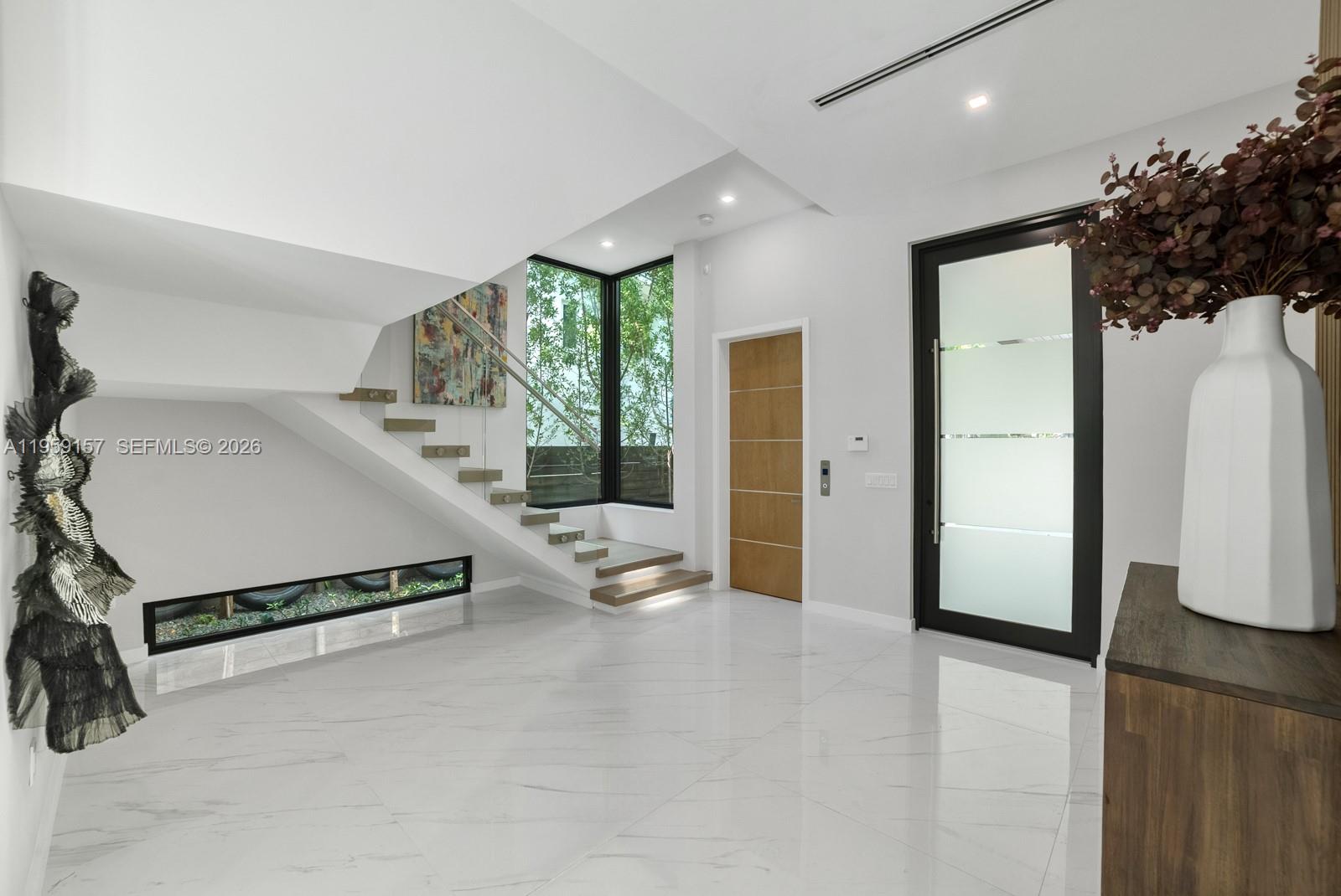 A modern foyer features white marble floors, a floating staircase, and a glass-paneled front door — 1780 Chucunantah Rd, Miami FL 33133, MIAMI, FL