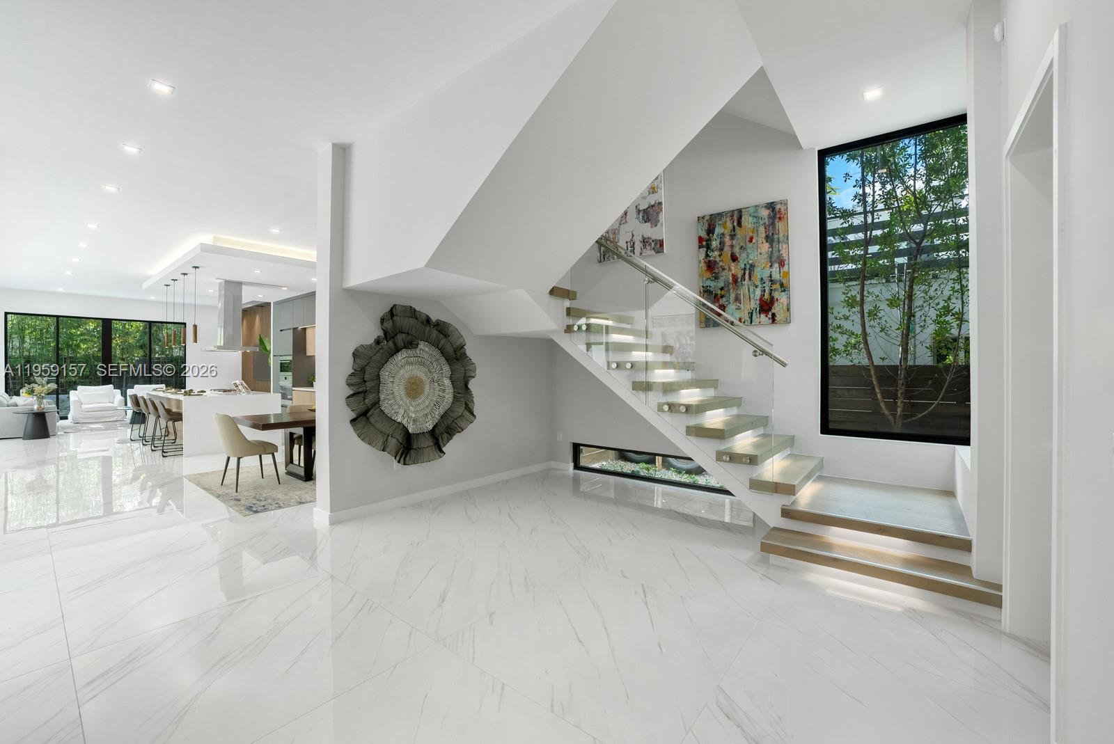 A modern open-concept interior features white marble floors, a floating staircase, and a kitchen area — 1780 Chucunantah Rd, Miami FL 33133, MIAMI, FL