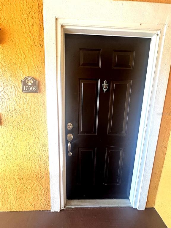 A dark brown front door with a silver knocker is set in a yellow wall — 5483 VINELAND ROAD UNIT 10309, ORLANDO, FL