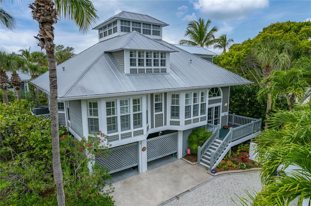 An elevated gray house with a metal roof, lattice garage doors, and a wooden staircase — 12 SEAWATCH DRIVE, BOCA GRANDE, FL