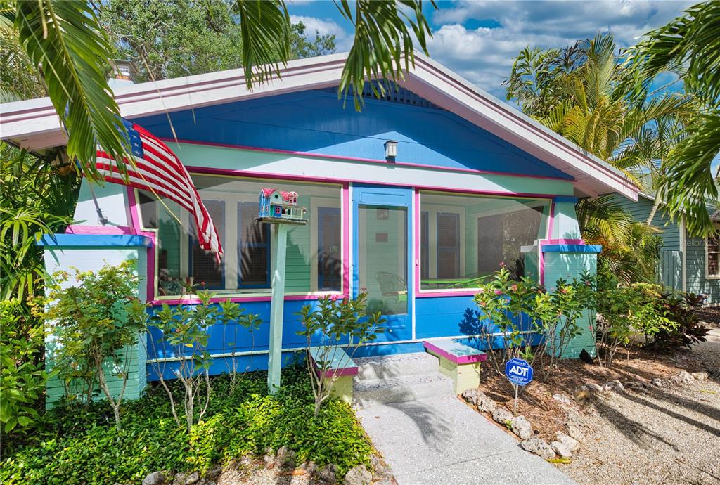 A colorful, single-story bungalow features a screened front porch, a birdhouse, and an American flag — 642 OHIO PLACE, SARASOTA, FL