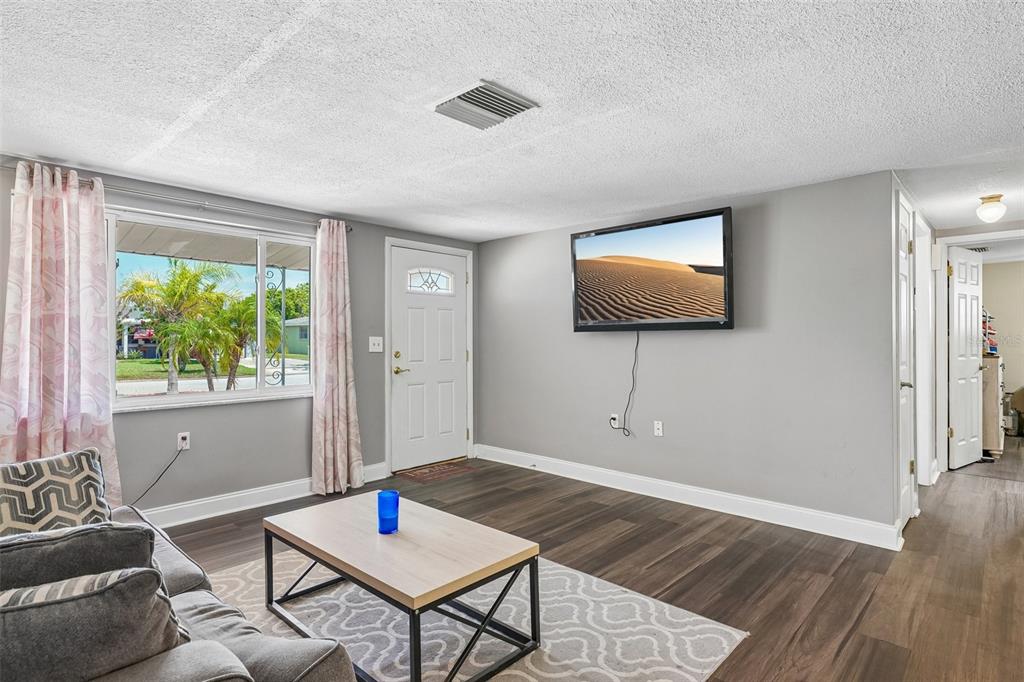 A living room features gray walls, wood-look flooring, a wall-mounted television, and a front door — 1133 GRAND BOULEVARD, HOLIDAY, FL
