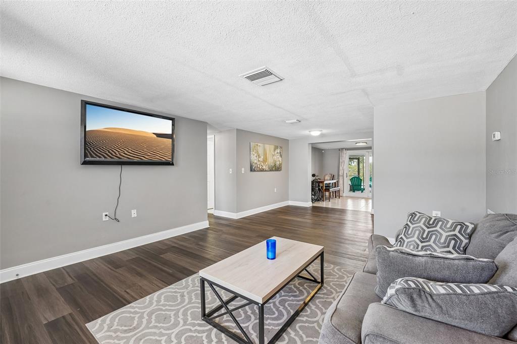A living room with gray walls, wood-look flooring, a wall-mounted television, and a gray sofa — 1133 GRAND BOULEVARD, HOLIDAY, FL