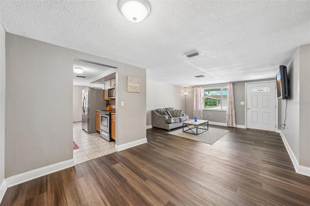 A living room with wood-look flooring opens into a kitchen with stainless steel appliances — 1133 GRAND BOULEVARD, HOLIDAY, FL