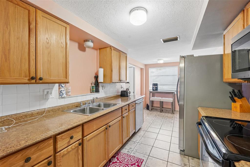 A kitchen features light wood cabinets, laminate countertops, a double sink, and tile flooring — 1133 GRAND BOULEVARD, HOLIDAY, FL