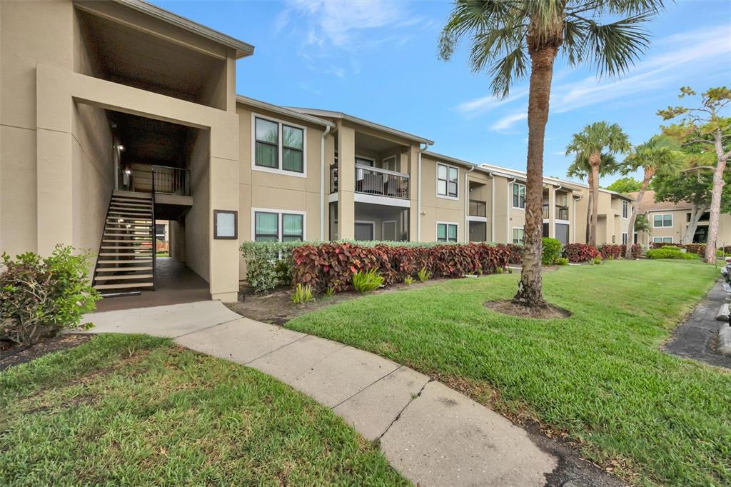 A tan apartment building exterior features a concrete walkway, outdoor stairs, and landscaped bushes — 4065 CROCKERS LAKE BOULEVARD UNIT 14, SARASOTA, FL