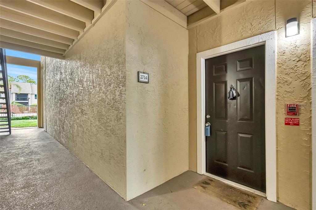 An exterior view of a residential apartment entrance with a dark door and stucco walls — 4065 CROCKERS LAKE BOULEVARD UNIT 14, SARASOTA, FL