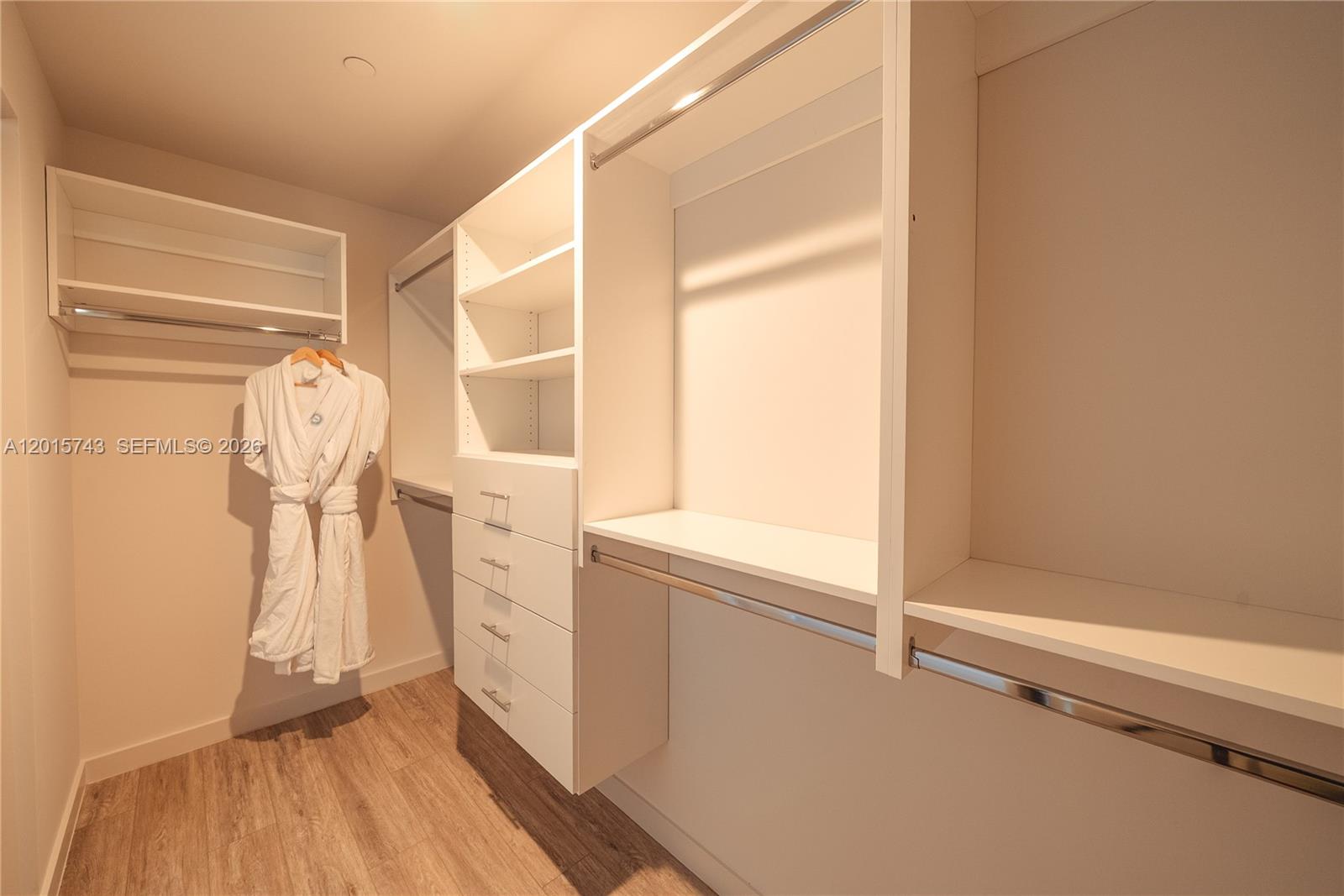 A walk-in closet features white shelving, a built-in dresser, hanging rods, and wood-look flooring — 275 SW 6th St # 5307, Miami FL 33130, MIAMI, FL