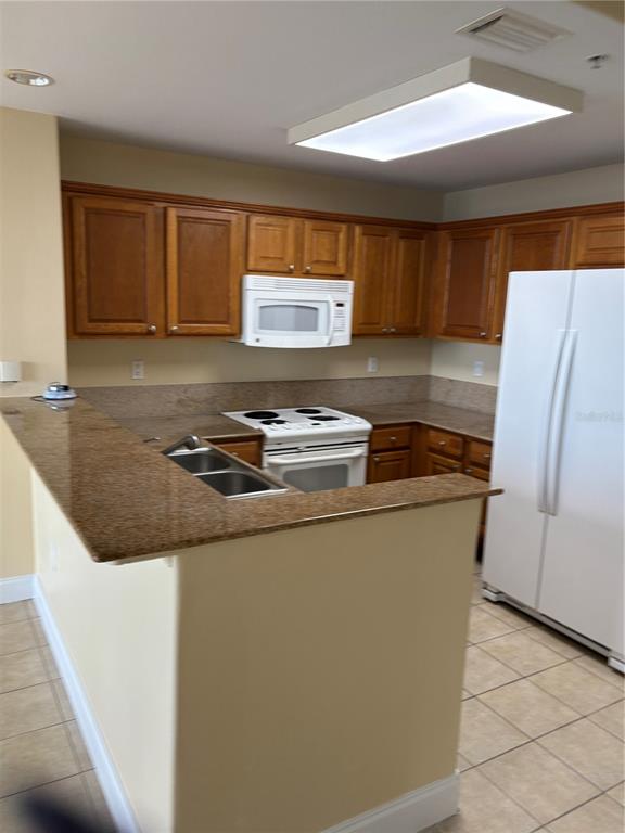 A kitchen features wood cabinets, granite countertops, white appliances, and a breakfast bar — 13427 BLUE HERON BEACH DRIVE UNIT 406, ORLANDO, FL
