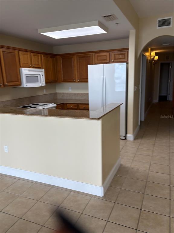 A kitchen features wood cabinets, granite countertops, a white refrigerator, and tile flooring — 13427 BLUE HERON BEACH DRIVE UNIT 406, ORLANDO, FL