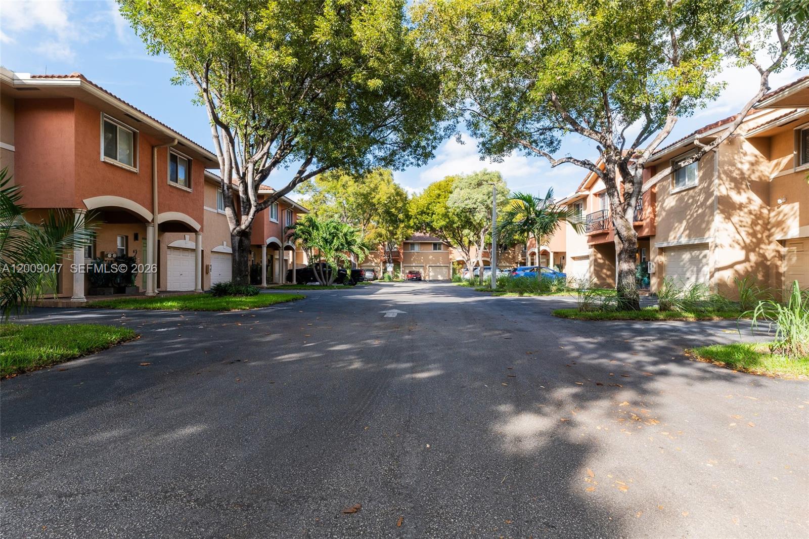 A paved driveway leads between two rows of multi-story residential townhouses with mature trees — 59 SE 3rd Ave # 59, Hallandale Beach FL 33009, HALLANDALE BEACH, FL