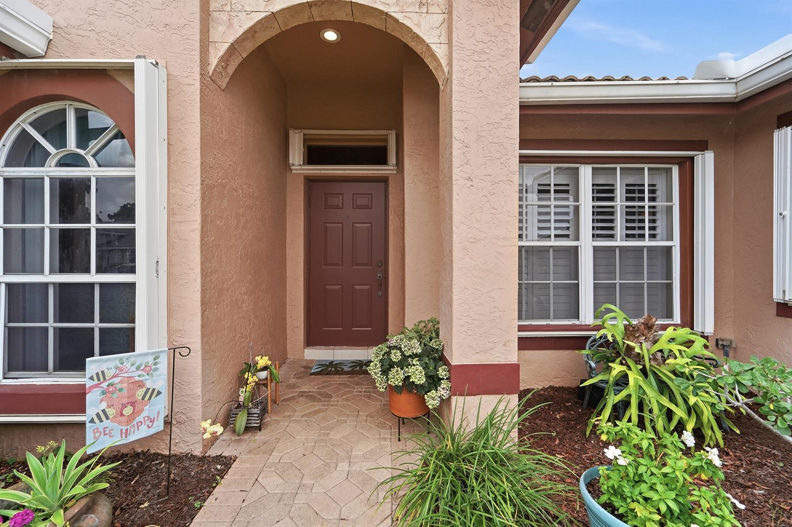 The exterior of a house features a brown front door, arched entryway, and landscaped garden — 4788 S Cypress Dr Drive S, Boynton Beach FL 33436, BOYNTON BEACH, FL
