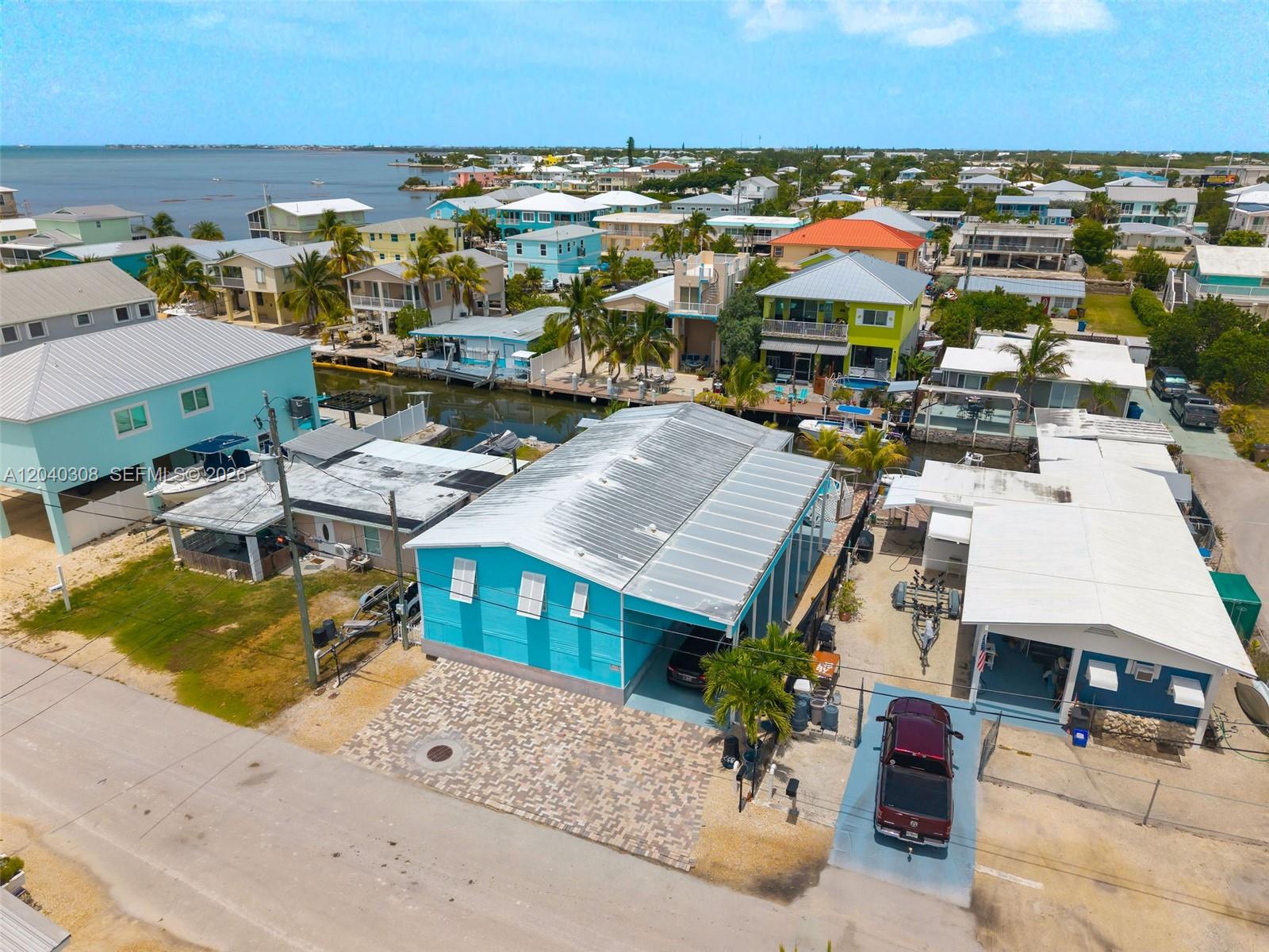 An aerial view shows a bright blue house with a metal roof and paved driveway — 837 91st Court Ocean, Marathon FL 33050, MARATHON, FL