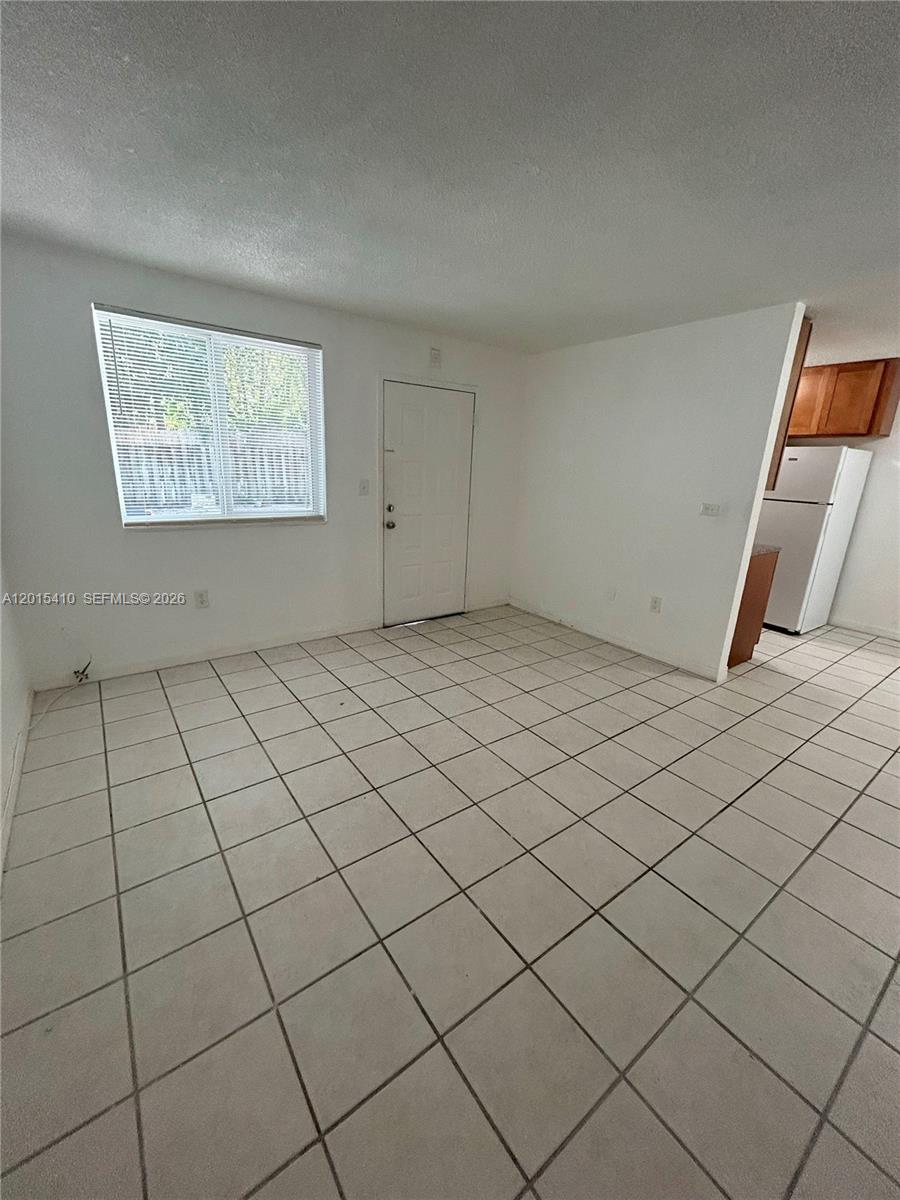 A room with white walls, tiled floors, a window with blinds, and an adjacent kitchen — 5814 NE 4th Ct # 3, Miami FL 33137, MIAMI, FL