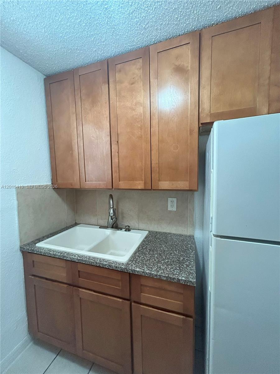 A small kitchen features wooden cabinets, a granite countertop, and a white double sink — 5814 NE 4th Ct # 3, Miami FL 33137, MIAMI, FL