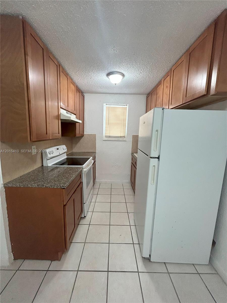 This galley-style kitchen features wood cabinets, granite countertops, white appliances, and tiled flooring — 5814 NE 4th Ct # 3, Miami FL 33137, MIAMI, FL