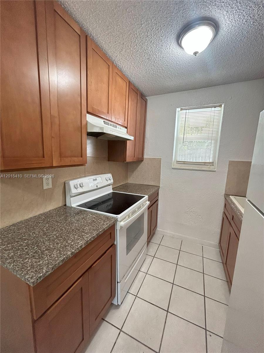A galley kitchen features wood cabinets, laminate countertops, white appliances, and tiled flooring — 5814 NE 4th Ct # 3, Miami FL 33137, MIAMI, FL