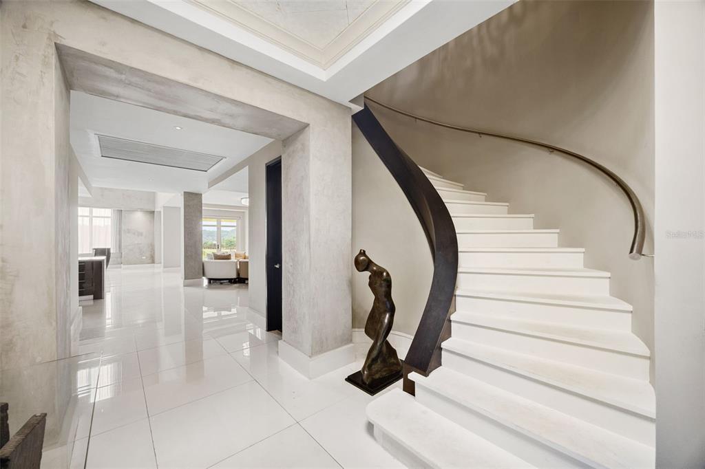 A modern foyer features a curved white staircase, a dark sculpture, and polished tile floors — Carr. 693 Km.10 HM 7 PLANTATION VILLAGE DRIVE UNIT 1202, DORADO, PR
