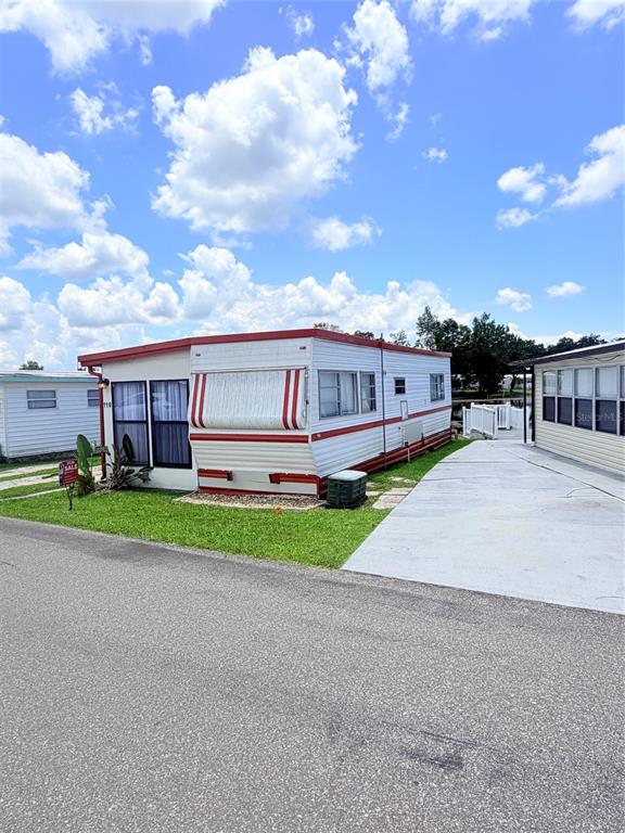 A white mobile home with red trim sits next to a paved driveway under a sky — 110 KOVE BOULEVARD, OSTEEN, FL
