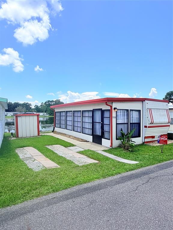 A single-story mobile home with a sunroom and a small shed sits on a grassy lot — 110 KOVE BOULEVARD, OSTEEN, FL