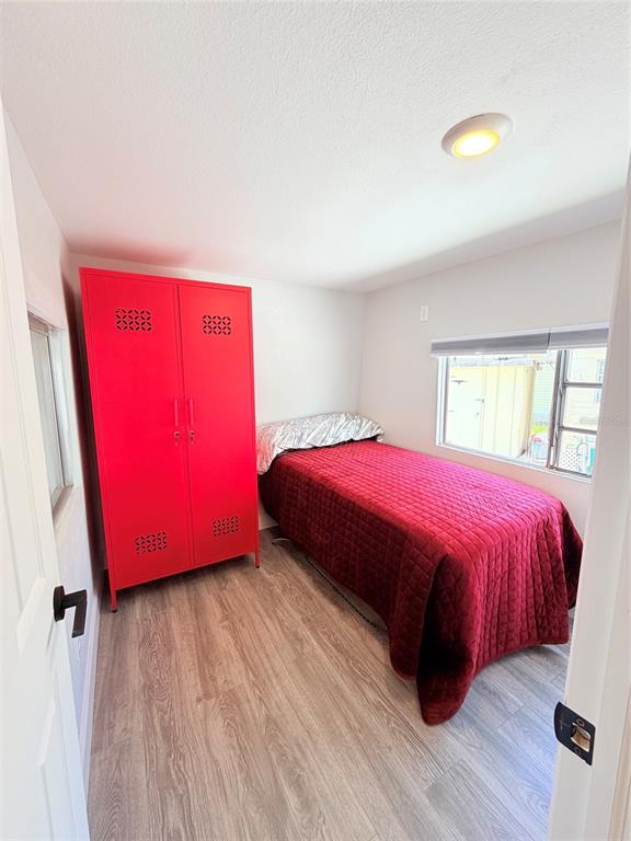 A bedroom features light wood-look flooring, a red metal locker, and a bed with red bedding — 110 KOVE BOULEVARD, OSTEEN, FL