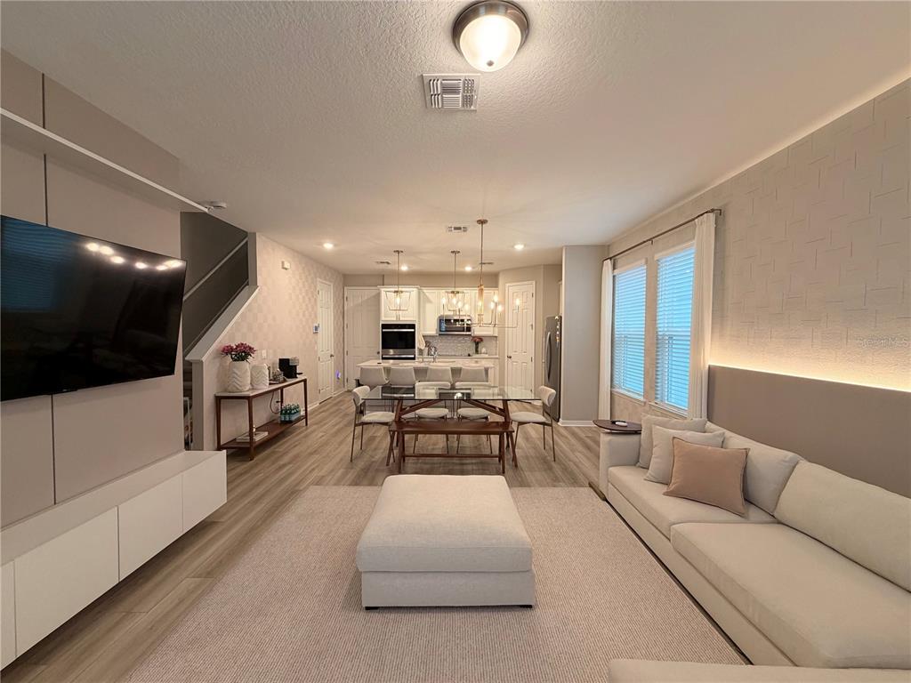 A modern open-concept living and dining area features light wood floors and neutral furniture — 4863 LACEWING DRIVE, WINTER GARDEN, FL