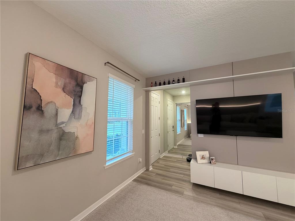 A living room features a wall-mounted television, a white media console, and abstract wall art — 4863 LACEWING DRIVE, WINTER GARDEN, FL