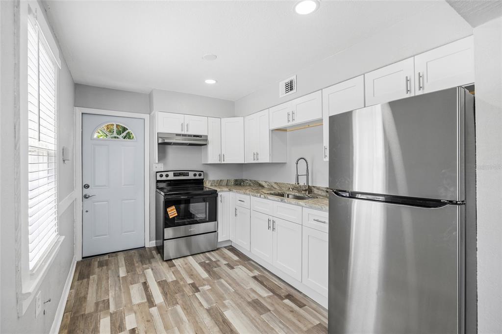 A kitchen features white cabinets, stainless steel appliances, and wood-look flooring — 128 W NORTH STREET, TAMPA, FL