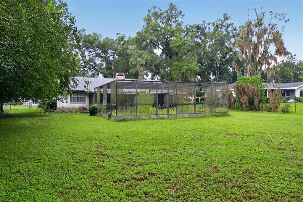 A backyard view of a house with a large screened-in porch and mature trees — 4279 E ARLINGTON STREET, INVERNESS, FL
