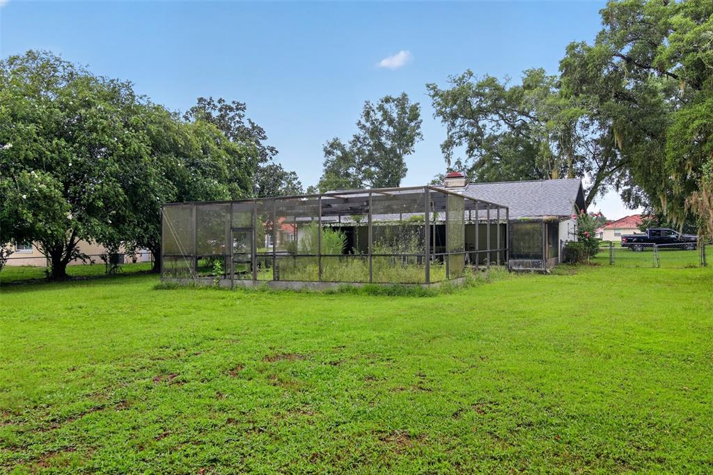A backyard view of a house featuring a large, overgrown screened-in patio enclosure — 4279 E ARLINGTON STREET, INVERNESS, FL