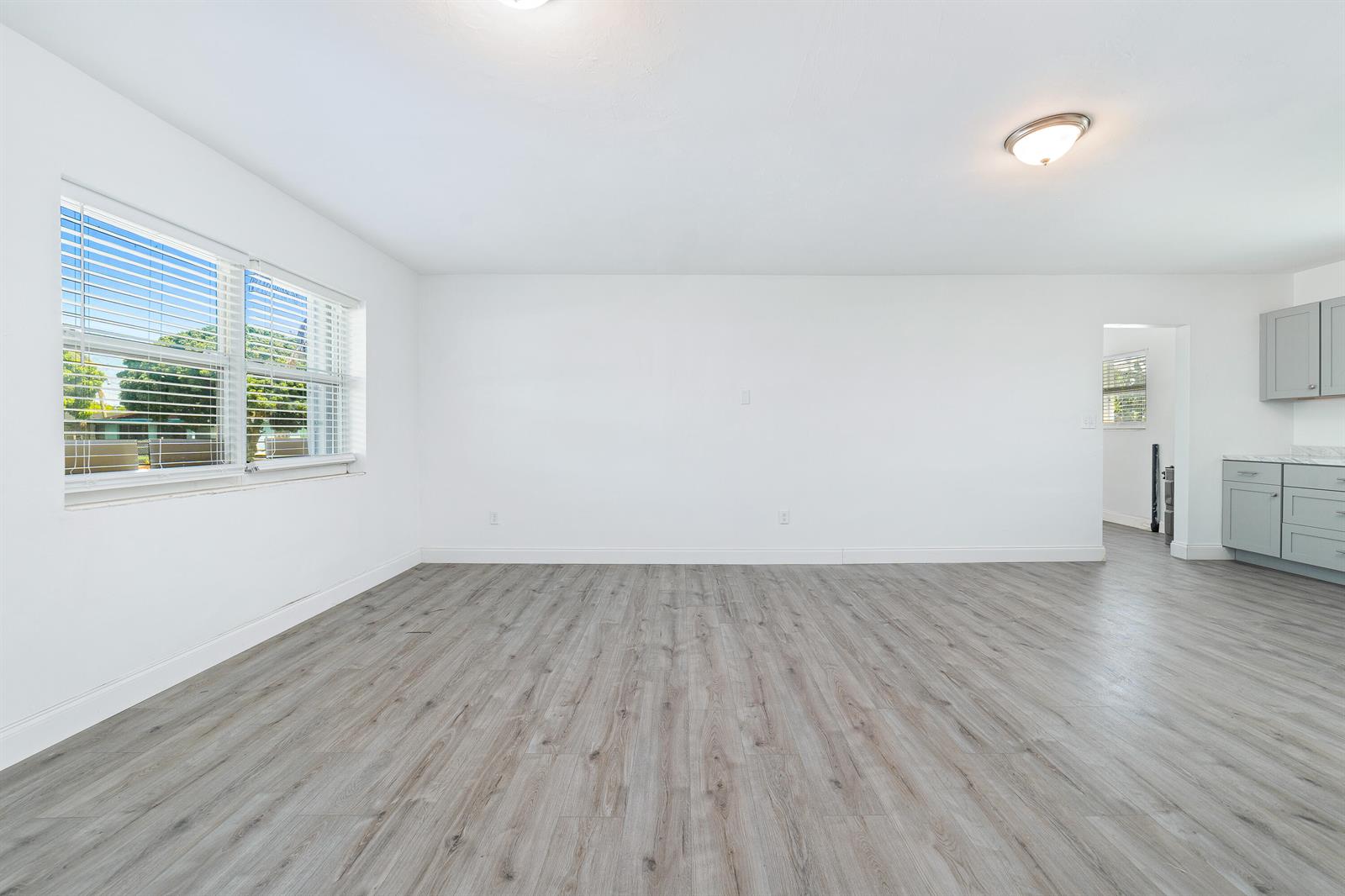 An empty room with light wood-look flooring, white walls, and a partial view of a kitchen — 317 NW 14th Street, Belle Glade FL 33430, BELLE GLADE, FL