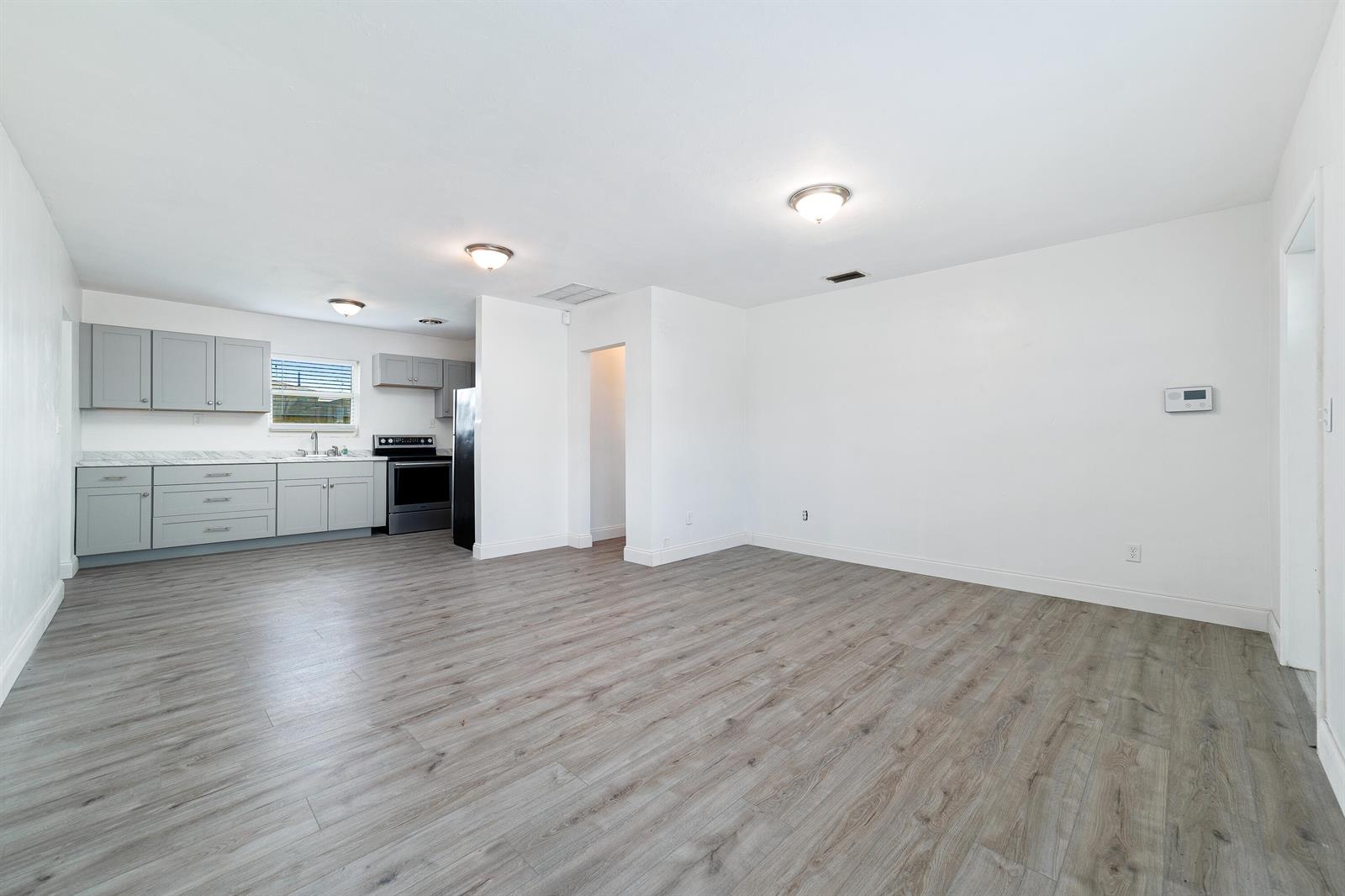 An open-concept kitchen and living area features gray cabinets, white walls, and wood-look flooring — 317 NW 14th Street, Belle Glade FL 33430, BELLE GLADE, FL