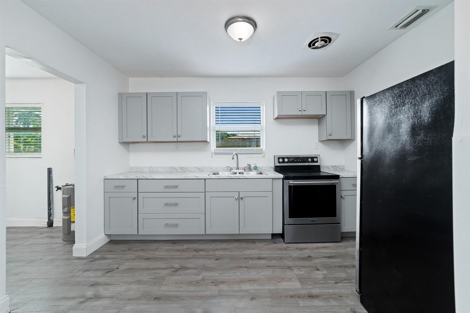 A kitchen features gray cabinets, marble-look countertops, stainless steel appliances, and wood-look flooring — 317 NW 14th Street, Belle Glade FL 33430, BELLE GLADE, FL