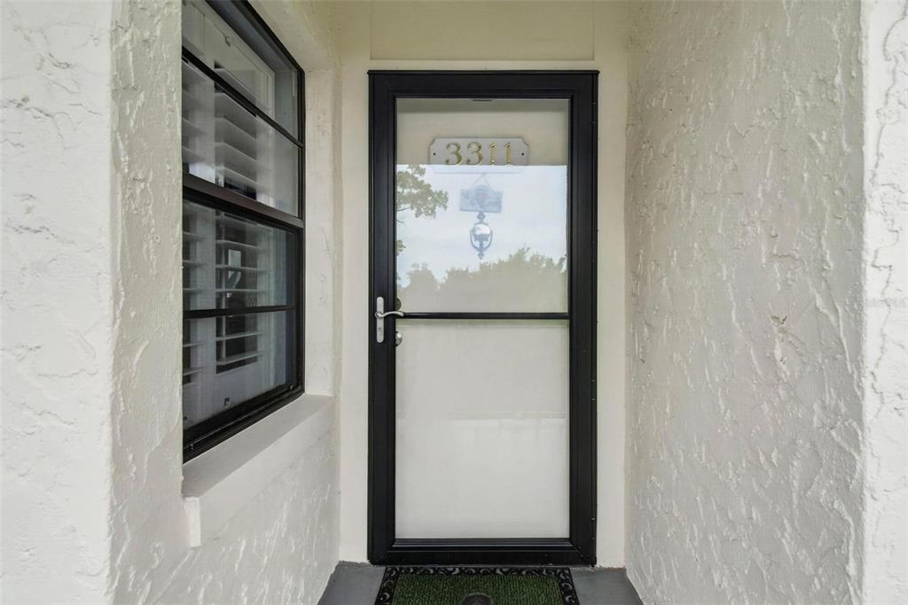A black storm door with the number 3311 sits in a white stucco entryway — 14130 ROSEMARY LANE UNIT 3311, LARGO, FL