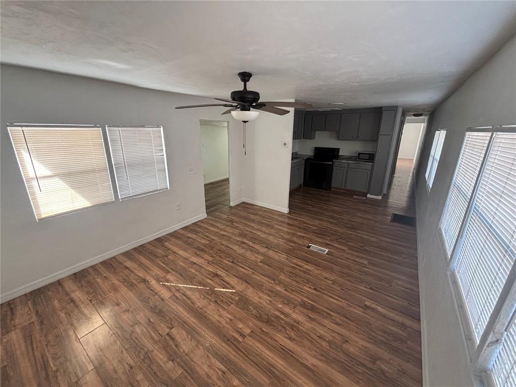 An open-concept living area features wood-look flooring, a ceiling fan, and an adjacent kitchen — 5480 PINELAND AVENUE, PORT ORANGE, FL