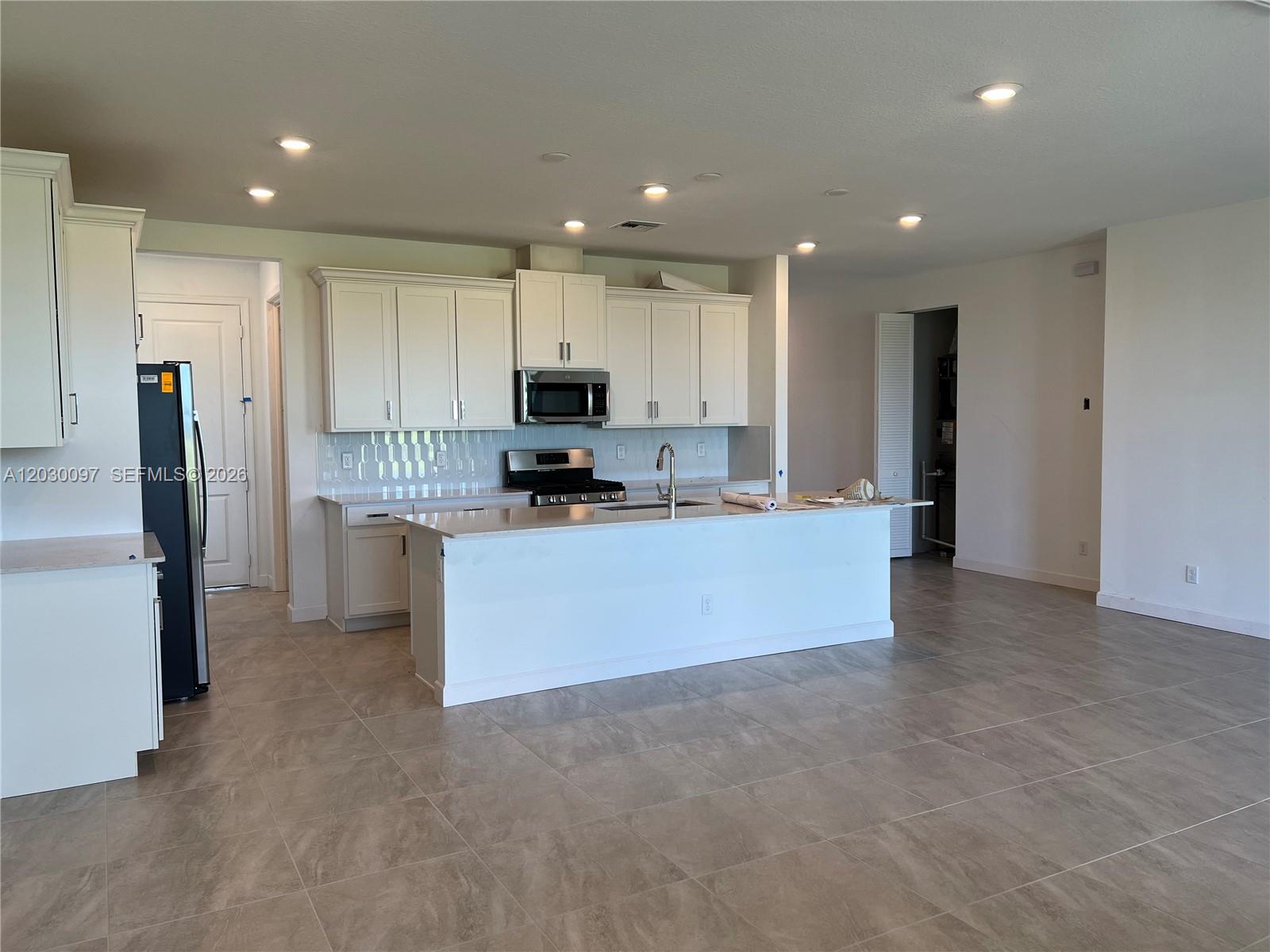 A modern kitchen features white cabinets, a central island, and light-colored tile flooring — 19667 Rugged Trunk Trl # 0, Loxahatchee FL 33470, LOXAHATCHEE, FL