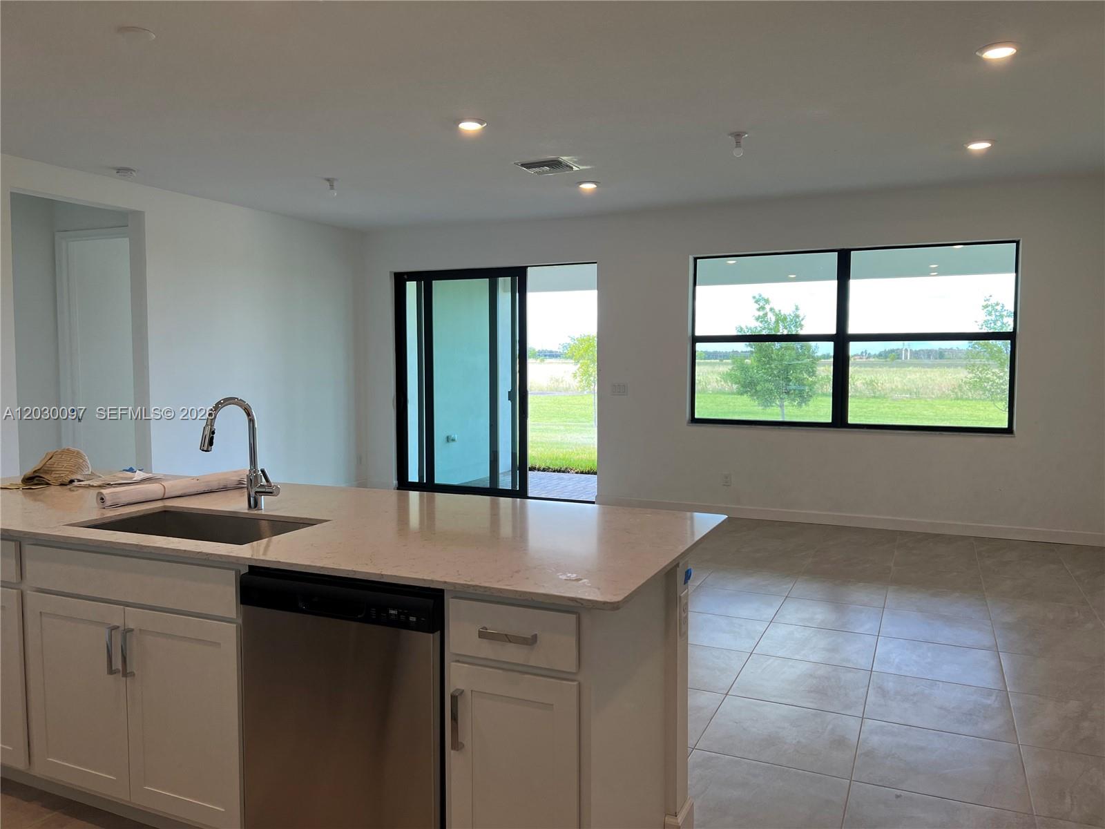 A kitchen island with a stainless steel sink overlooks an open living area with windows — 19667 Rugged Trunk Trl # 0, Loxahatchee FL 33470, LOXAHATCHEE, FL