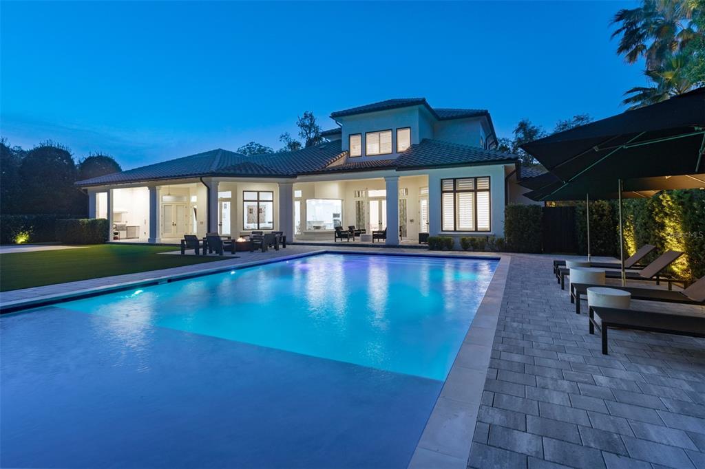 A modern house exterior at dusk features a large illuminated swimming pool and patio area — 1180 VIA LUGANO, WINTER PARK, FL