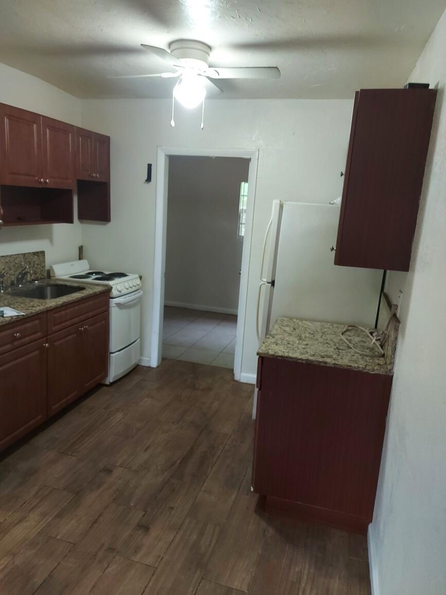 A kitchen with dark wood cabinets, granite countertops, white appliances, and wood-look flooring — 1980 Lincoln Avenue, Opa-Locka FL 33054, OPA-LOCKA, FL