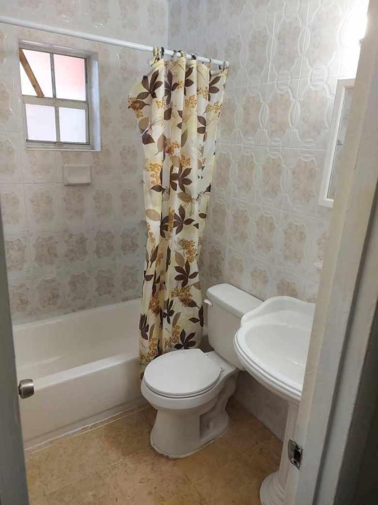 A small bathroom featuring a pedestal sink, a toilet, and a tub with a shower curtain — 1980 Lincoln Avenue, Opa-Locka FL 33054, OPA-LOCKA, FL
