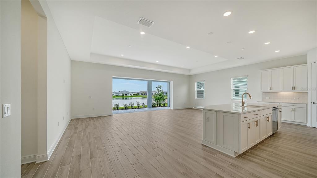 An open-concept kitchen and living area features light wood-look tile floors and a water view — 14406 SKIPPING STONE LOOP, PARRISH, FL
