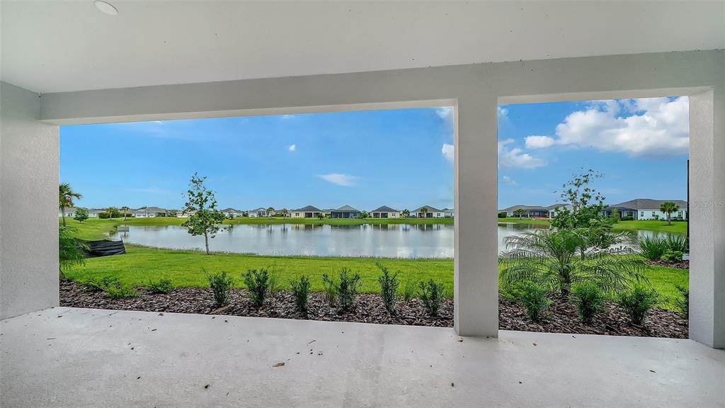 A covered concrete patio overlooks a grassy lawn, a pond, and a neighborhood of houses — 14406 SKIPPING STONE LOOP, PARRISH, FL