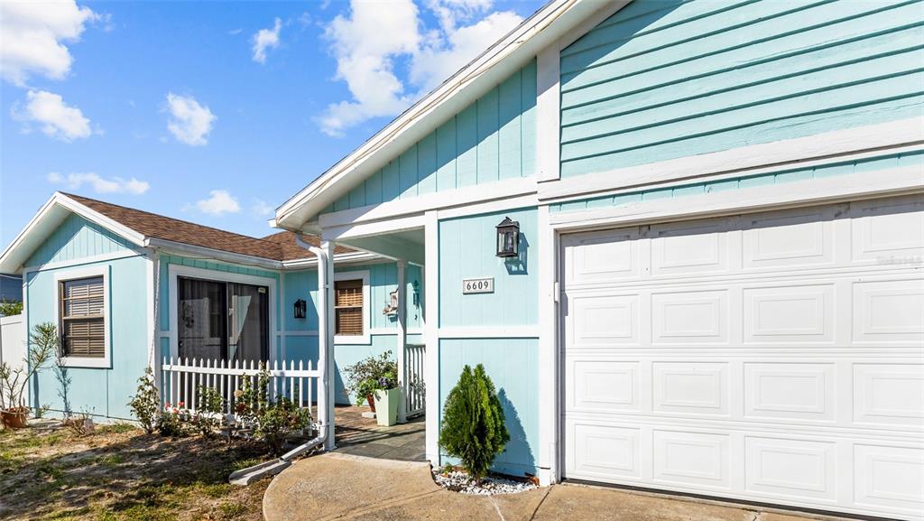 A light blue house exterior features a white garage door, a small porch, and landscaping — 6609 MAUNA LOA BOULEVARD, SARASOTA, FL