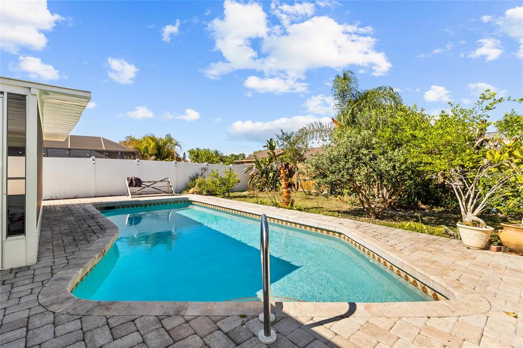 A backyard features a rectangular swimming pool surrounded by a paver patio and white fencing — 6609 MAUNA LOA BOULEVARD, SARASOTA, FL