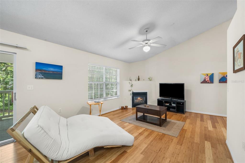 A living room features a fireplace, a ceiling fan, wood flooring, and a white futon — 10000 SW 52ND AVENUE UNIT 77, GAINESVILLE, FL