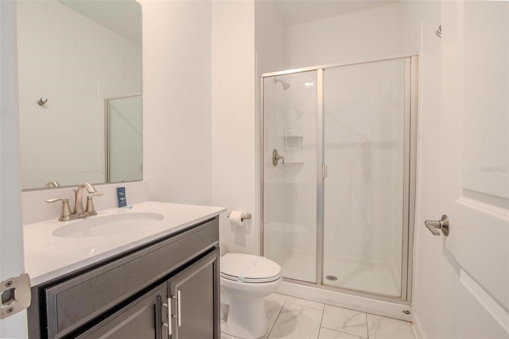 A bathroom features a dark vanity, white countertop, toilet, and a glass-enclosed shower stall — 962 SPLASH SHOT PLACE, DAVENPORT, FL