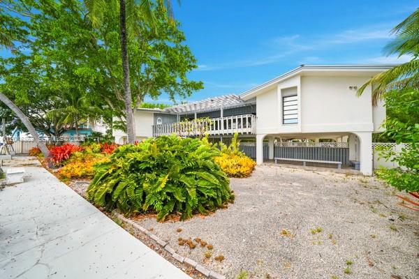 An elevated white house with a balcony stands above a gravel yard with tropical plants — 154 Redwing Rd, Tavernier FL 33070, TAVERNIER, FL