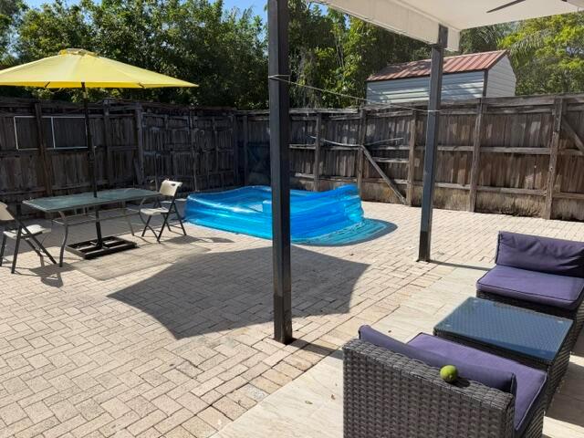 A paved backyard patio features a dining set with a yellow umbrella and a small pool — 4357 NW 6 Avenue, Deerfield Beach FL 33064, DEERFIELD BEACH, FL