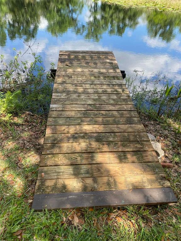 A wooden dock extends from a grassy bank into a calm pond — 1135 N JACKADEE POINT, INVERNESS, FL