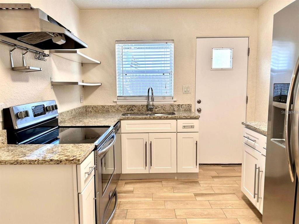A kitchen features white cabinets, granite countertops, stainless steel appliances, and wood-look flooring — 2510 BOYD AVENUE UNIT B, ORLANDO, FL